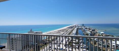 A coastal view from a balcony overlooking a beach, a marina, and a cityscape.