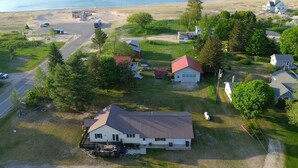 A large house with a garage, surrounded by a grassy area and trees, near a beach.