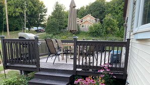 A deck with outdoor furniture, a small garden with pink flowers, and a house in the background.