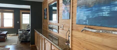 A room with wooden paneling, a kitchen counter, and a large painting of a lake.