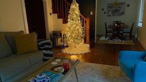 Un saló amb un arbre de Nadal, un sofà, una taula de centre amb llibres i una espelma, i una zona de menjador amb cadires i una taula.