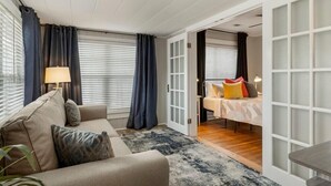 A modern hotel room with a sofa, a small table, a lamp, and a bed with colorful pillows. - The Enchanting Home @TU & Cherry Street (Tulsa)