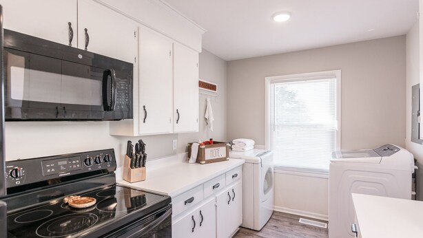 A compact kitchen with a black stove, a microwave, white cabinets, a washing machine, and a dryer. - Cozy House in Gallatin City Limits (Gallatin)
