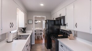 A modern kitchen with white cabinets, a black refrigerator, and a dining area with a white table and chairs. - Cozy House in Gallatin City Limits (Gallatin)