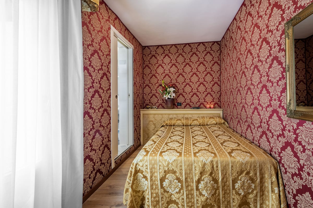 A bedroom with a large bed, a nightstand with a vase of flowers, and a mirror on the wall.