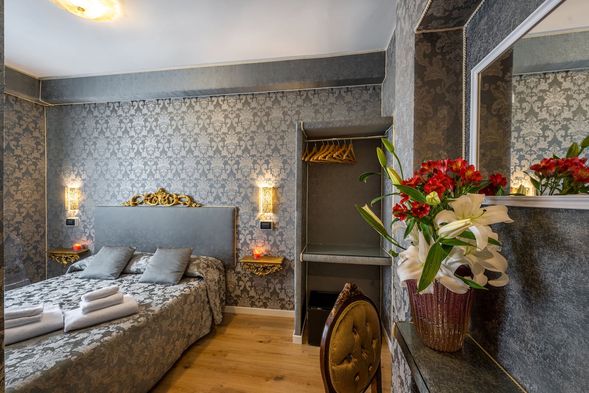 A bedroom with a bed, bedside tables, a mirror, and a fireplace.