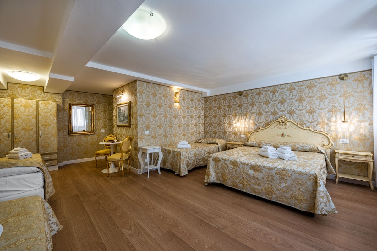 A hotel room with two beds, a small table, a chair, and a nightstand with a lamp.