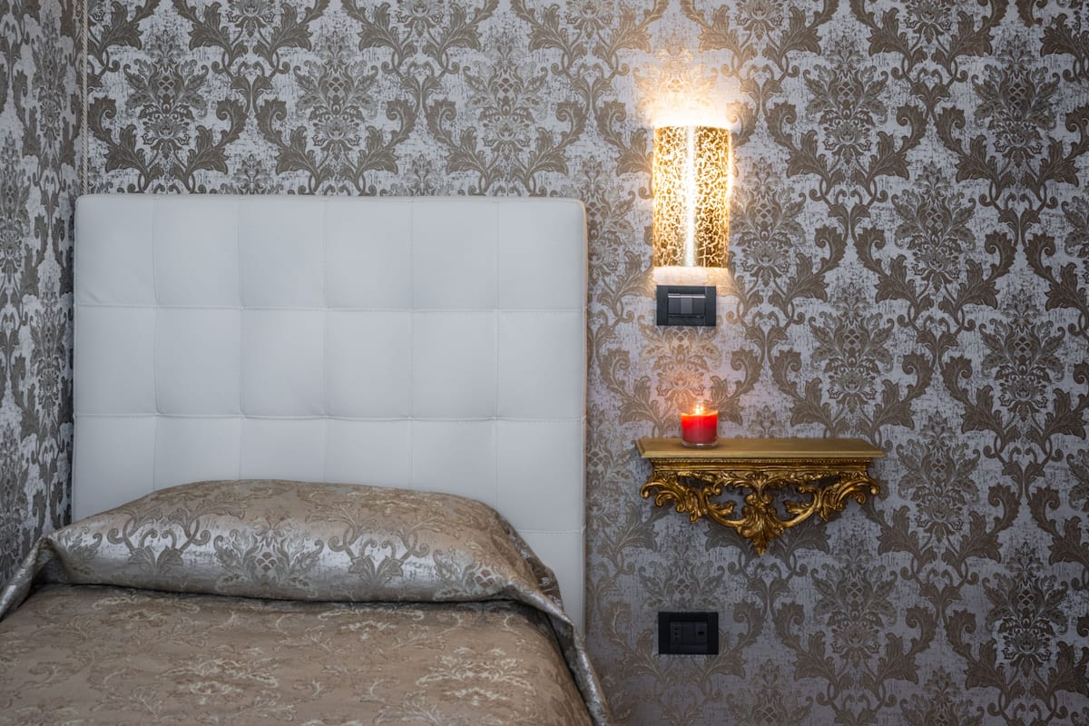 A bedroom with a tufted headboard, a bedside table with a candle, and ornate wall sconces.