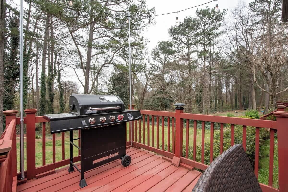 Een barbecue op een houten terras met een rode balustrade, omringd door bomen.