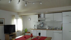 A compact kitchen with white cabinets, a wooden countertop, and a dining area with a red tablecloth. - Vacation apartment for a relaxing vacation (Argenbühl)