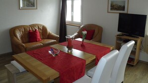 A furnished room with a wooden table, two leather sofas, a TV, and framed pictures on the walls. - Vacation apartment for a relaxing vacation (Argenbühl)