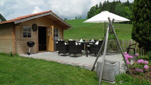 A wooden cabin with a patio area, a grill, and outdoor seating. - Vacation apartment for a relaxing vacation (Argenbühl)