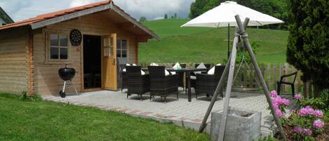 Een houten chalet met een terras, een barbecue en zitplaatsen buiten.