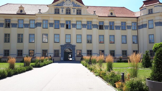 A large, symmetrical building with a central entrance, flanked by symmetrical wings, and surrounded by manicured gardens. - Vacation apartment for a relaxing vacation (Argenbühl)