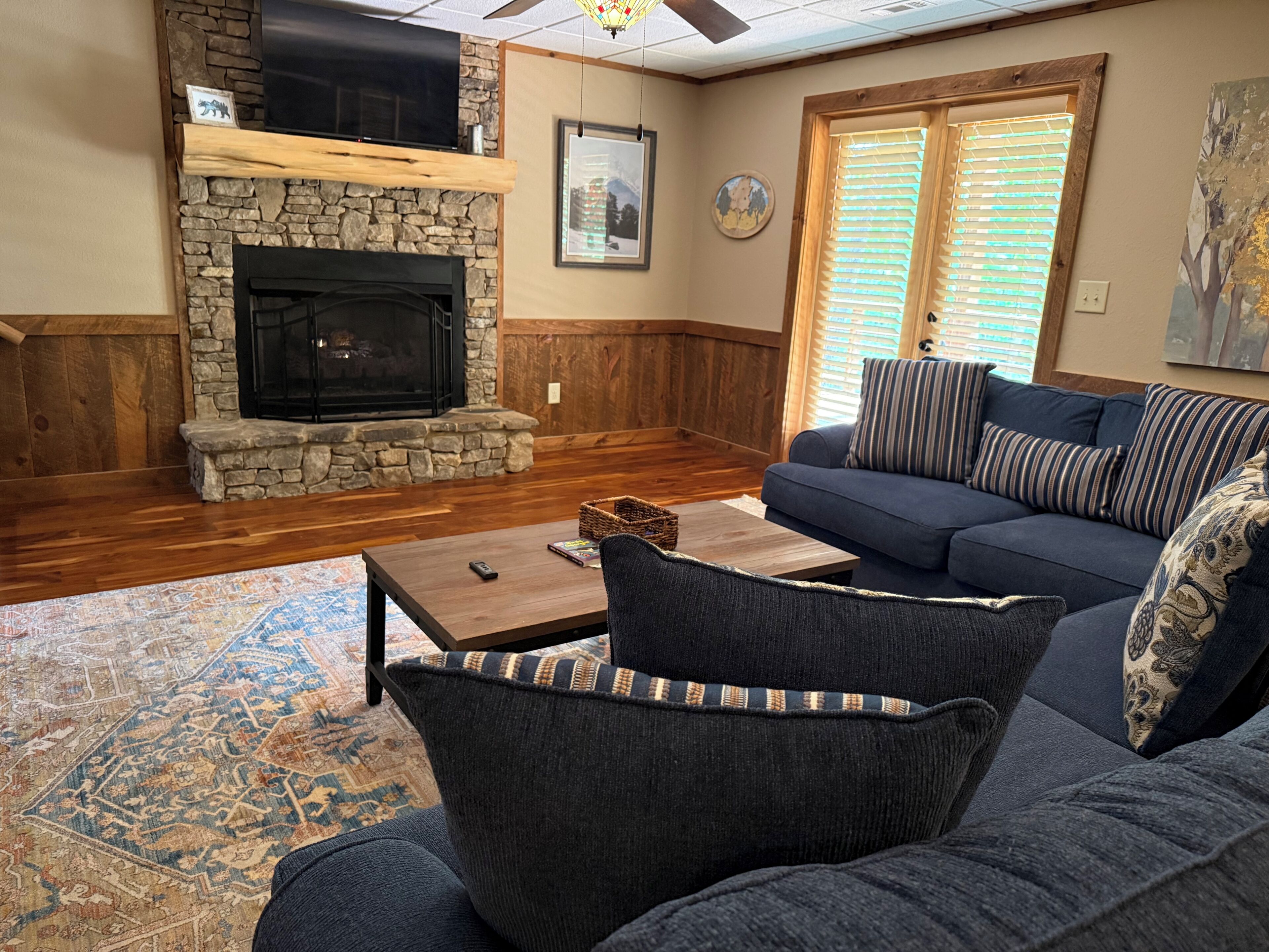 A living room with a stone fireplace, a blue sofa, a coffee table, and a patterned rug.