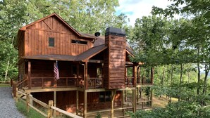 Une cabane en bois dotée d’un balcon et d’une cheminée, entourée d’arbres.