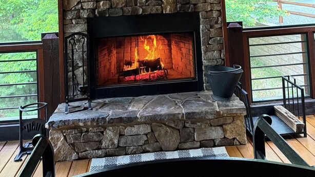 Une cheminée en pierre avec un feu, une cheminée en bois et une fenêtre au-dessus.