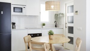 Una cocina moderna con armarios blancos, un refrigerador negro, microondas, estufa, pileta y comedor con una mesa redonda de madera y dos sillas.