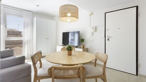Una sala de estar moderna con una mesa redonda de madera, cuatro sillas de madera, un sofá, un televisor y un gran ventanal con cortinas.