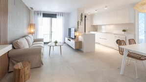 A modern living room with a sofa, a coffee table, and a TV. There is a kitchen area with a dining table and chairs. - Amazing holidays in this  New condo mediterranean style. Wifi - only families (Playa de Gandía)