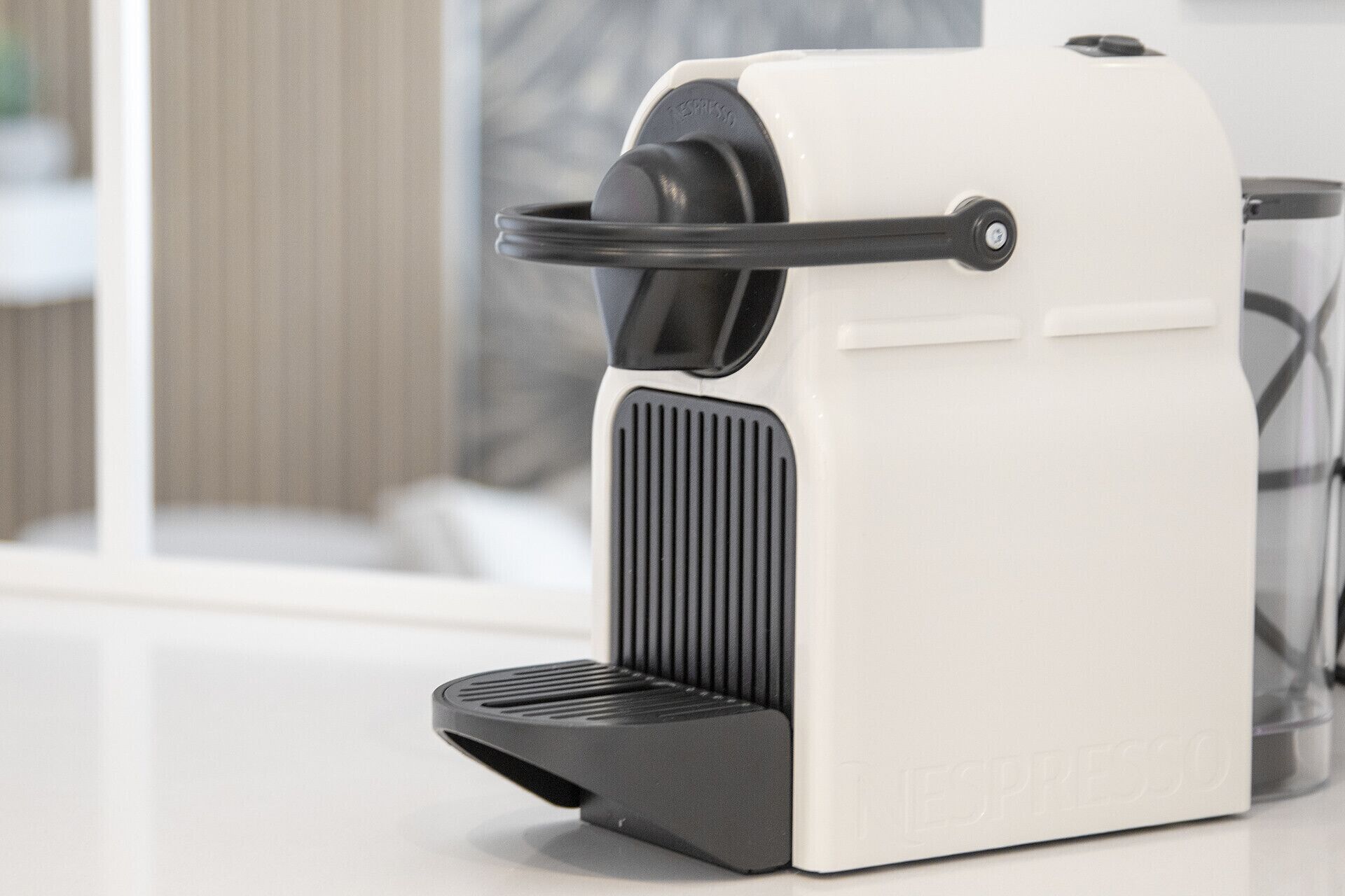 Eine weiße Espressomaschine mit schwarzem Griff und schwarzem Sockel, stehend auf einer weißen Arbeitsplatte.