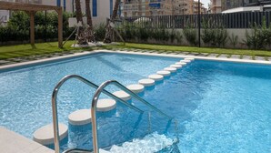 Una piscina con agua azul cristalina, una pérgola de madera y una escalera metálica que da a la piscina.