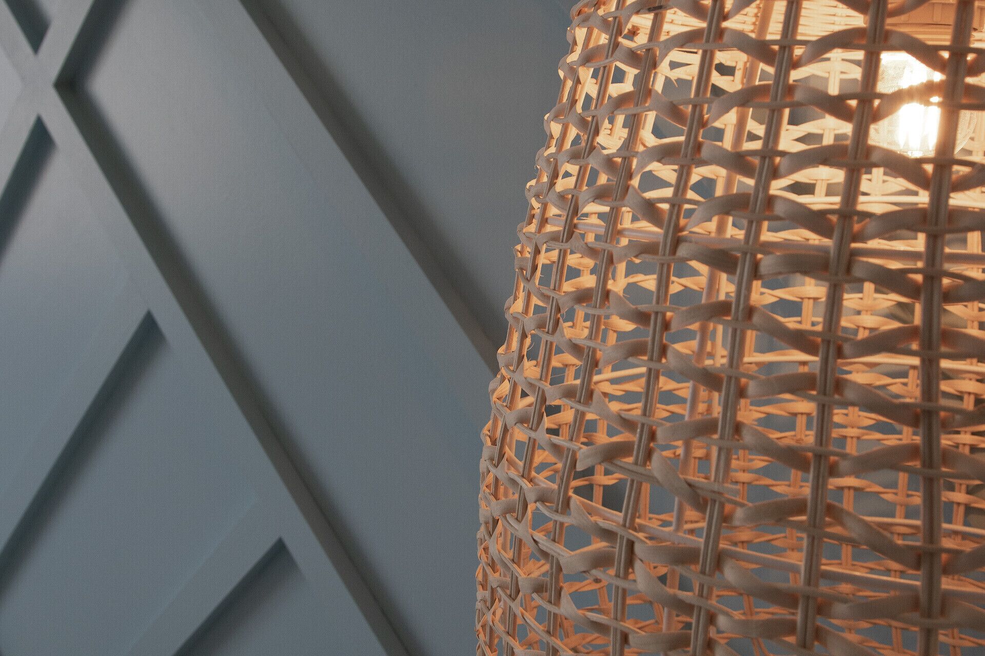 Gros plan d’un luminaire tissé, avec un motif géométrique sur le mur en arrière-plan.