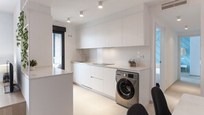 Una cocina moderna con muebles blancos, lavadora integrada y una pequeña ventana con persianas.