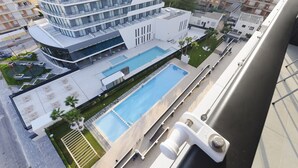 A modern building with a rooftop pool, surrounded by greenery and adjacent to other buildings.