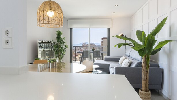 A modern living room with a large window, a dining area, and a grey sofa.
