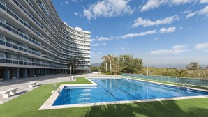 Un hotel moderno con fachada curva, piscina y vistas a montañas distantes.
