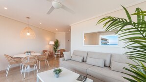 Una sala moderna con un sofá blanco, sillas de mimbre, una mesa de centro blanca y un ventilador de techo.