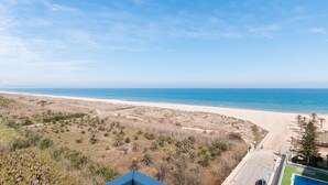 Vista de playa con cielo despejado, arena y vegetación escasa.