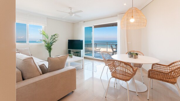 Una sala de estar moderna con un sofá, una mesa de comedor con sillas, un televisor y vistas a la playa.