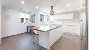 Una cocina moderna con muebles blancos, una isla grande y vistas a la ciudad a través de las ventanas.