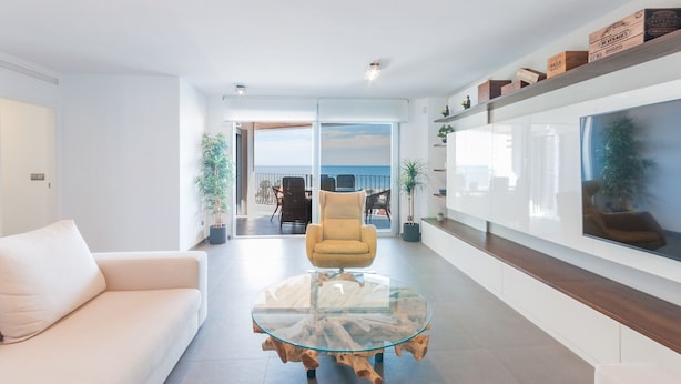Una sala de estar moderna con una mesa de centro de vidrio, un sillón amarillo y vista al mar a través de amplios ventanales.