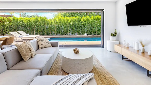 Ein modernes Wohnzimmer mit Blick auf einen Pool, inklusive Sofa, Couchtisch und Wandfernseher.