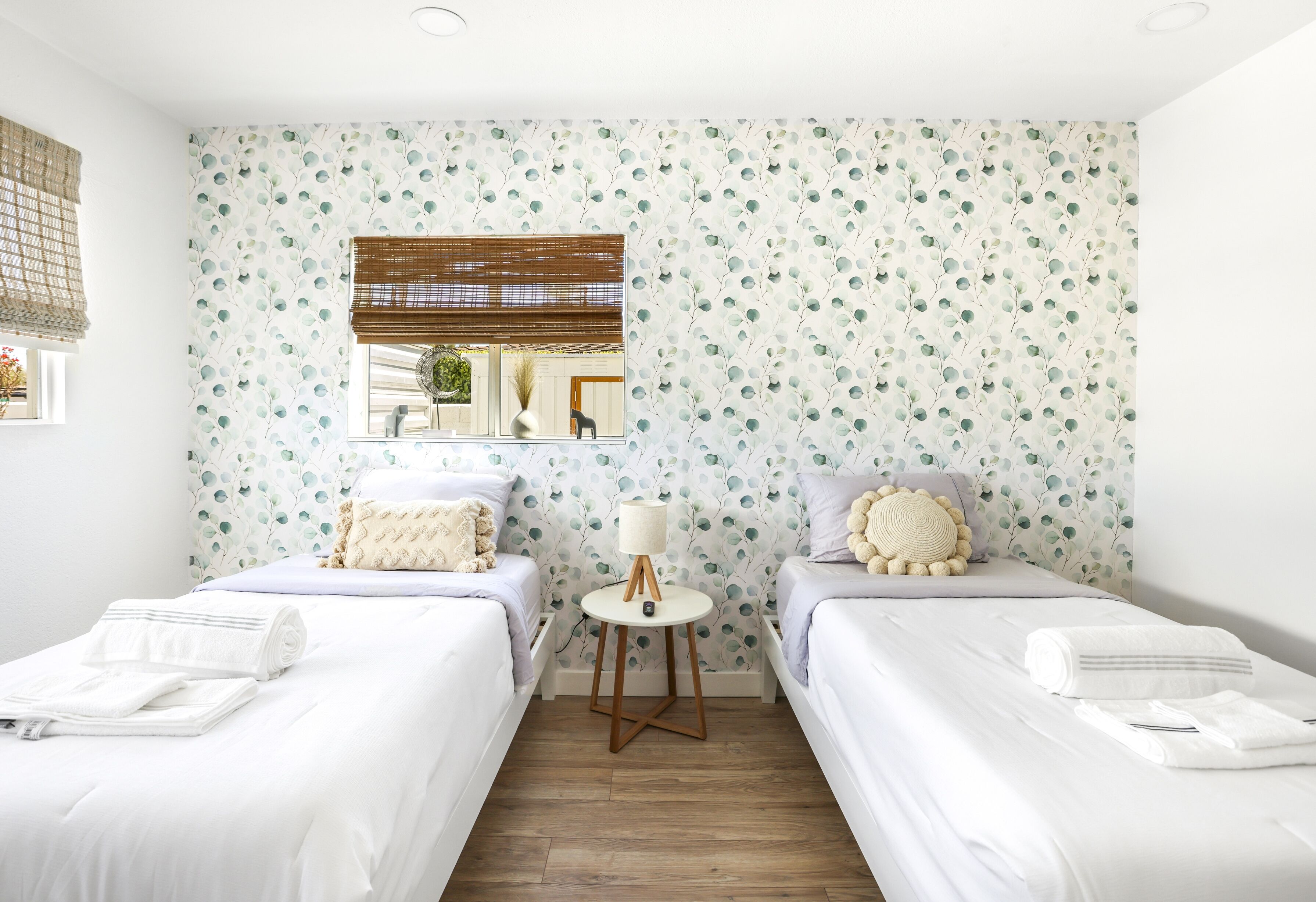 A hotel room with two single beds, a small table with a lamp, and a mirror on the wall.