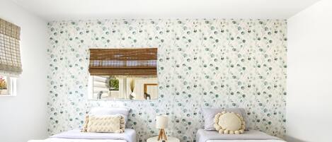 A hotel room with two single beds, a small table with a lamp, and a mirror on the wall.