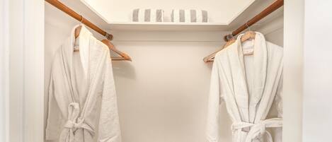 A walk-in closet with two white robes hanging on wooden racks, a wooden ceiling, and a white wall.