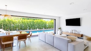 Ein modernes Wohnzimmer mit Blick auf einen Pool, einer Essecke und einem an der Wand befestigten Fernseher.