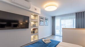 Ein modernes Hotelzimmer mit einem Bett, einem an der Wand befestigten Fernseher, einer kleinen Ablage mit Dekoration und einem großen Fenster mit Vorhängen.