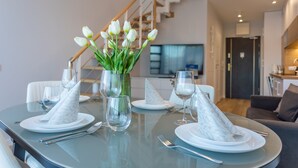 Ein Esstisch, gedeckt mit weißen Tellern, Servietten und Besteck, mit einer Vase voller weißer Tulpen in der Mitte.