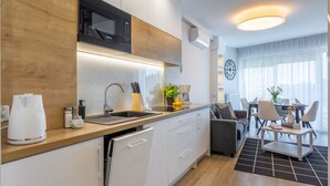 Eine moderne Küche mit weißen Schränken, einer schwarzen Mikrowelle und einer Holz Arbeitsplatte. Es gibt einen Essbereich mit Tisch und Stühlen sowie ein Wohnzimmer mit Sofa und Couchtisch.