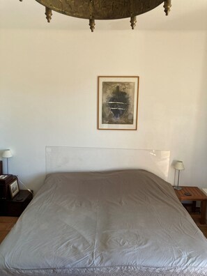 Ein Schlafzimmer mit einem großen Bett, einem gerahmten abstrakten Gemälde an der Wand und einem Nachttisch mit einer Lampe.