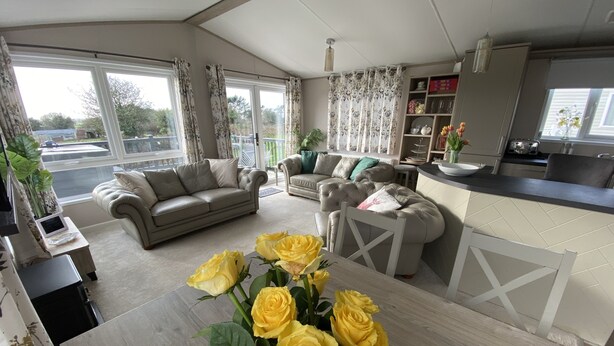 A modern living room with a sofa, a dining table with yellow roses, and a kitchen area. - Twilight Lodge & Hot Tub (2 Bd rm) 2.5 miles to beach, peaceful setting. (Truro)