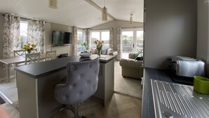 A modern kitchen with a central island, a dining area with a table and chairs, a sofa, and a TV mounted on the wall. - Twilight Lodge & Hot Tub (2 Bd rm) 2.5 miles to beach, peaceful setting. (Truro)
