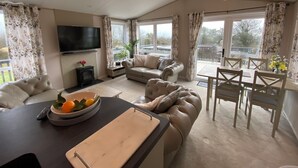 A spacious living room with a sofa, a dining table, and a TV. - Twilight Lodge & Hot Tub (2 Bd rm) 2.5 miles to beach, peaceful setting. (Truro)