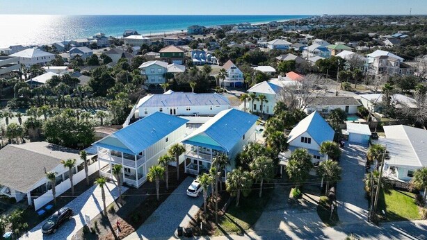 An aerial view of a coastal residential area with houses, some with blue roofs, and a clear view of the ocean. - Large Deck/ in-law suite /Walk to Beach/ Location! (Panama City Beach)