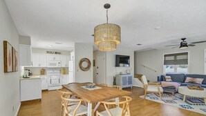 A modern kitchen with white cabinets, a wooden dining table, and a wicker pendant light. - Large Deck/ in-law suite /Walk to Beach/ Location! (Panama City Beach)
